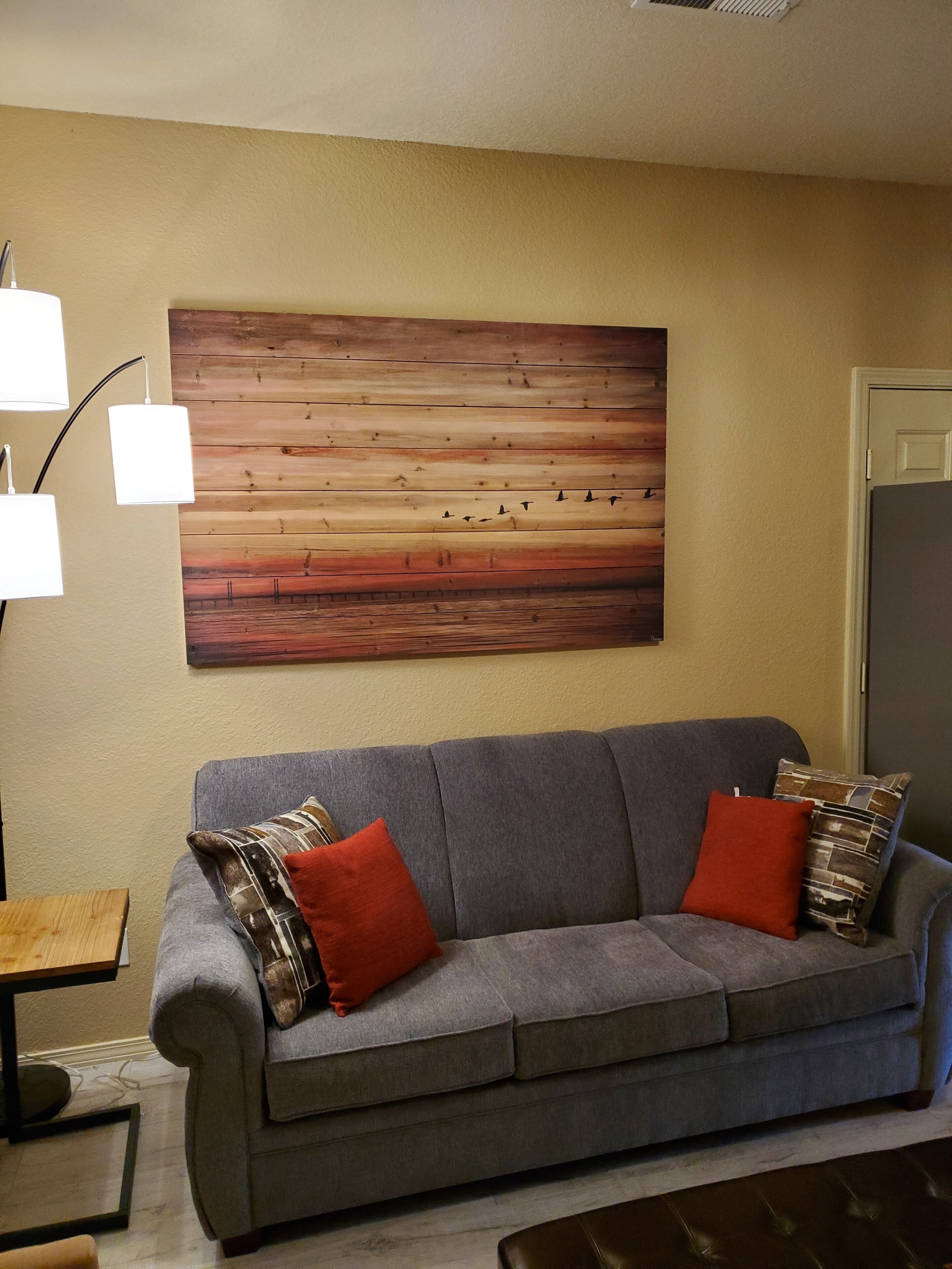 A living room with a grey sofa, two red cushions, a wooden wall panel, and a floor lamp.