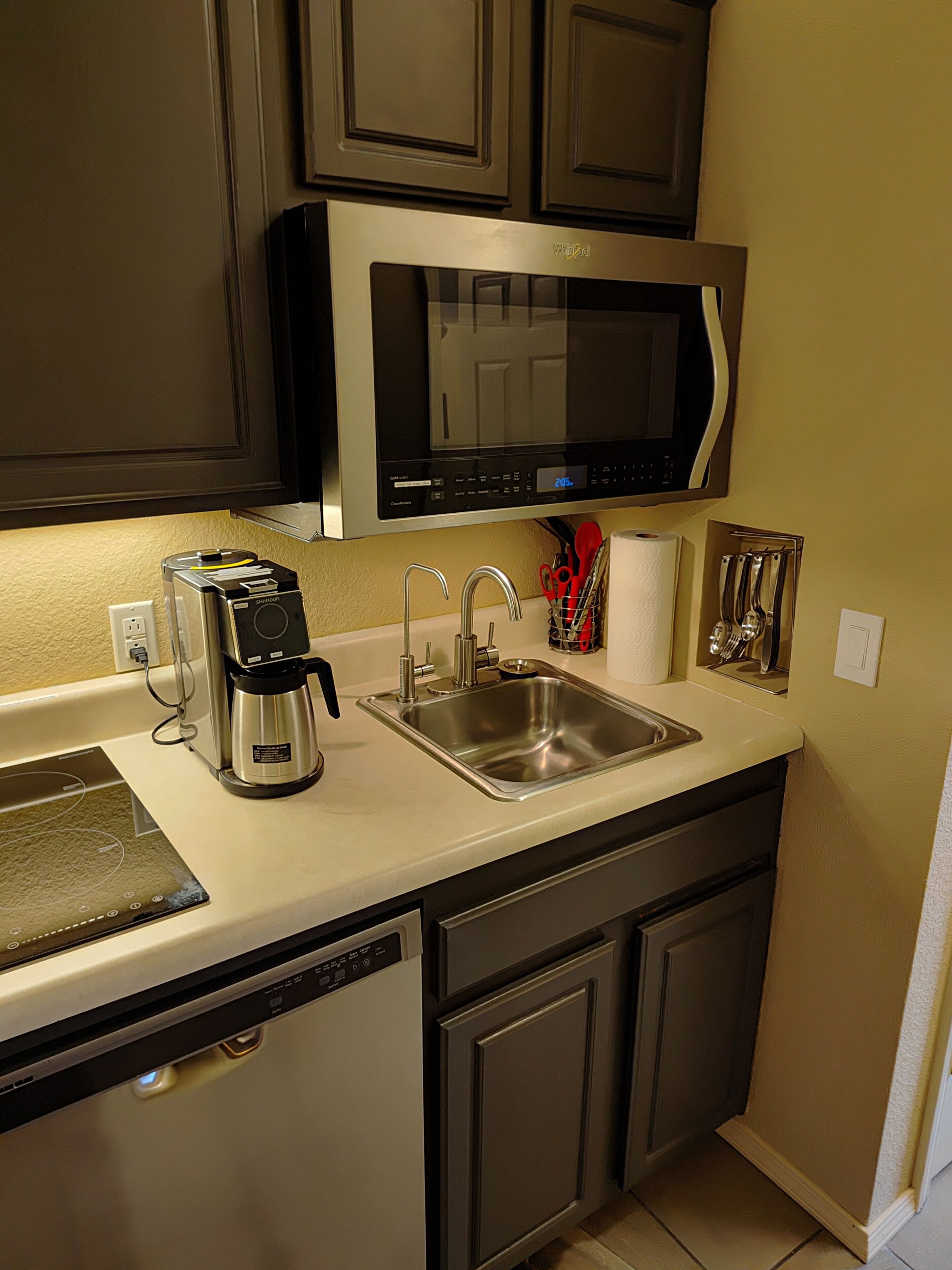 Cocina compacta equipada con microondas, cafetera, fregadero y lavavajillas.