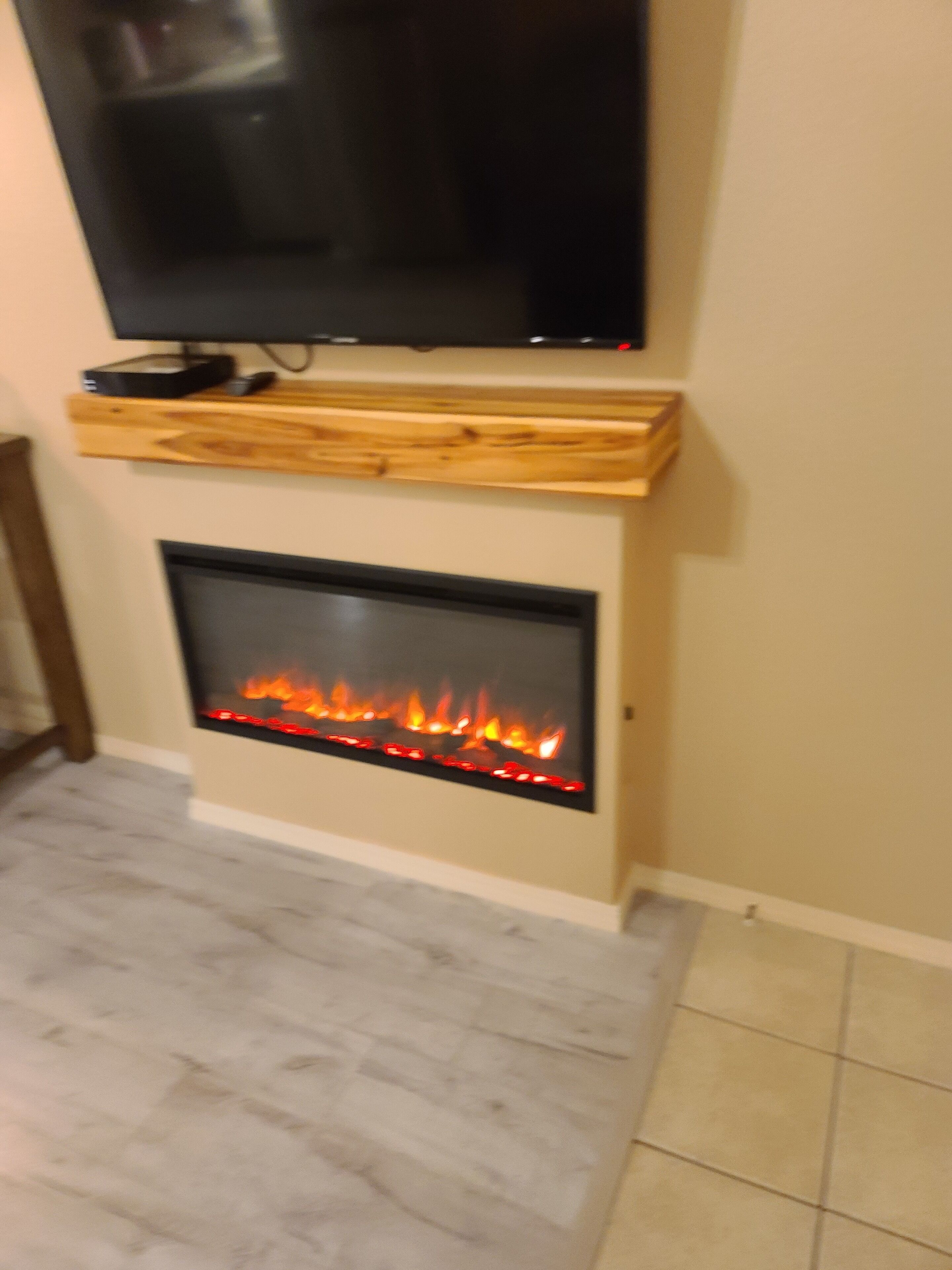 Una sala de estar moderna con un televisor de pantalla plana sobre una chimenea con fuego visible.