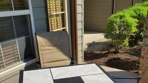 A patio area with a table and chairs, a small garden, and a building with large windows. - One bedroom resort condo on Golf Course with pool. 10 minutes to SDC! (Branson West)