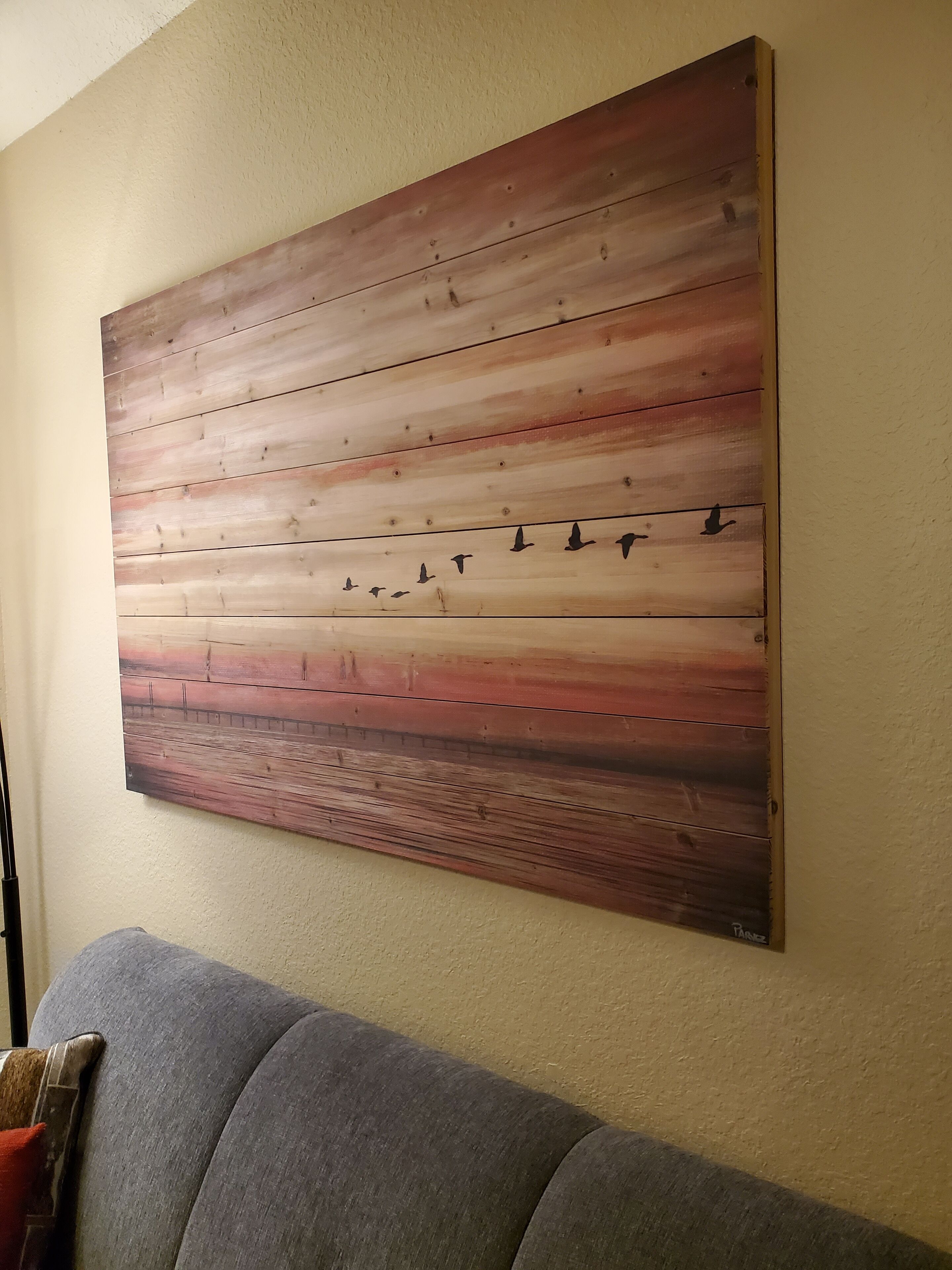 A large wooden wall art with a gradient from light to dark brown, featuring silhouettes of birds.