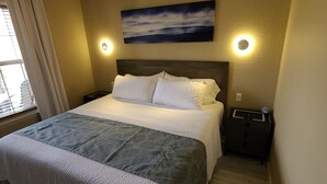 A hotel room with a large bed, a nightstand, a wall-mounted painting, and a window with curtains. - One bedroom resort condo on Golf Course with pool. 10 minutes to SDC! (Branson West)