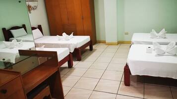 A hotel room with two single beds, a wooden wardrobe, a desk with a chair, and a mirror.