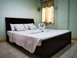 Una cama bien tendida con sábanas y almohadas blancas, y una toalla dispuesta en forma de corazón, junto a un cabecero de madera oscura.