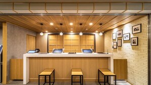 A reception area with a wooden counter, three stools, and a wall with framed pictures. - Super Hotel Yamaguchi Yuda Hot Springs (Yamaguchi)