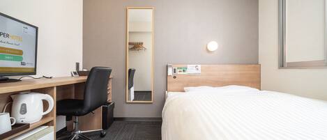 Una habitación de hotel con una cama, un escritorio con un ordenador, un hervidor y un espejo.