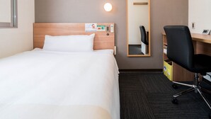 A hotel room with a bed, a desk, a chair, a mirror, and a wall-mounted light. - Super Hotel Yamaguchi Yuda Hot Springs (Yamaguchi)
