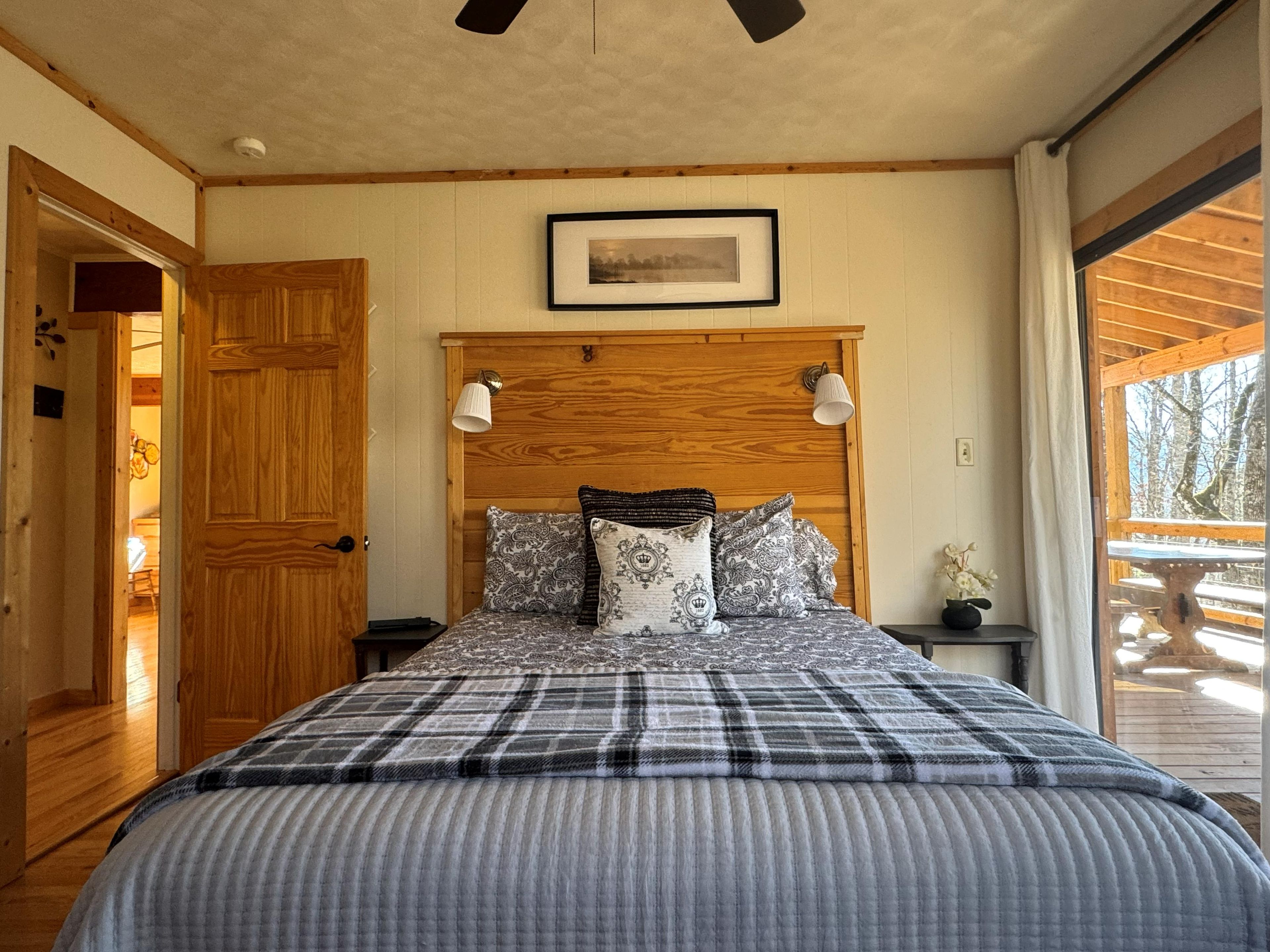 A bedroom with a wooden headboard, a bed with patterned bedding, two bedside lamps, and a framed picture on the wall.