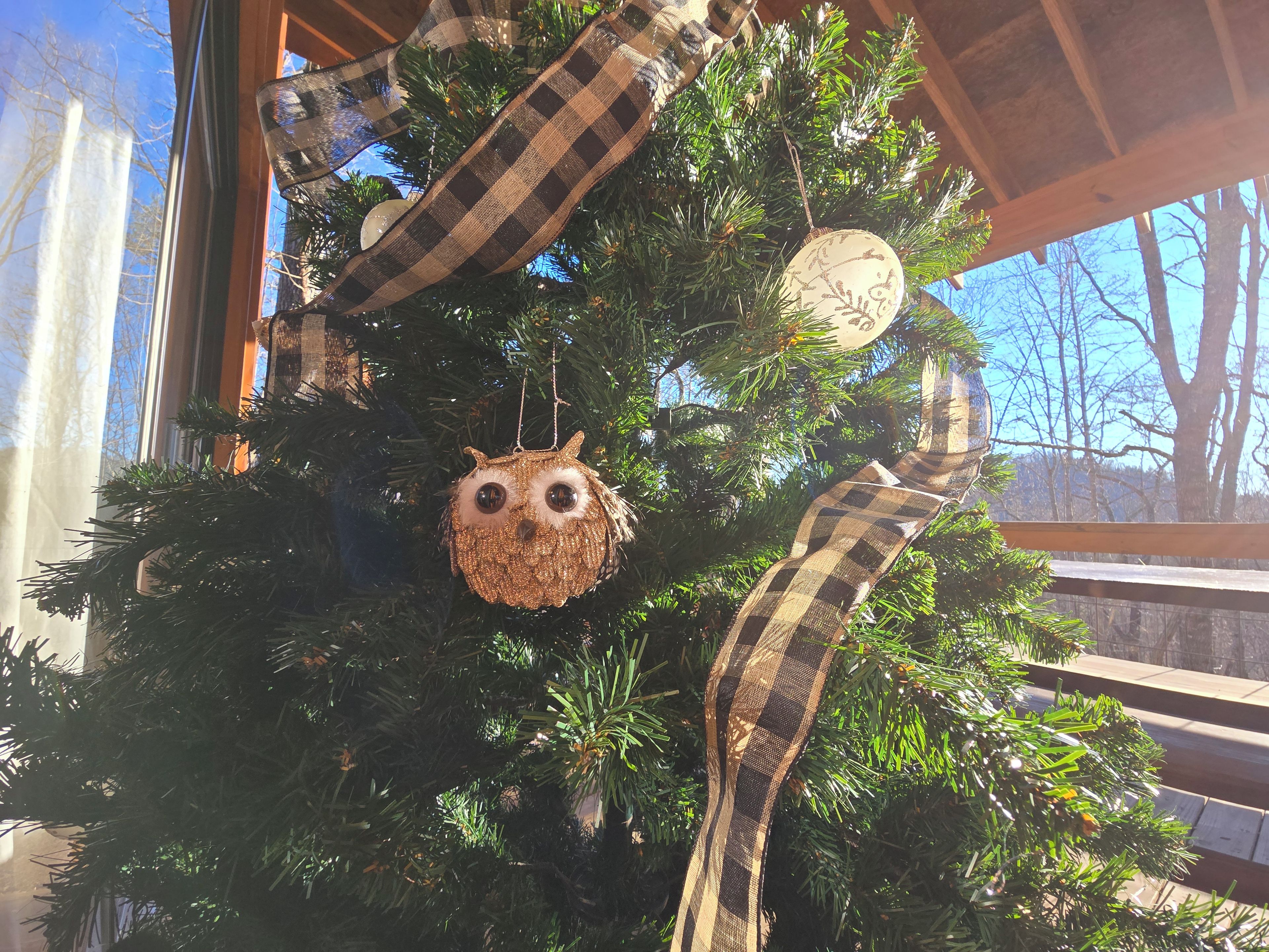 Ein Weihnachtsbaum mit einem karierten Band und einer Eule als Weihnachtsdeko.