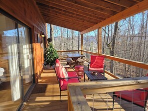 Una terraza de madera con puerta de cristal, un árbol de Navidad, sillas rojas y una mesa de picnic.