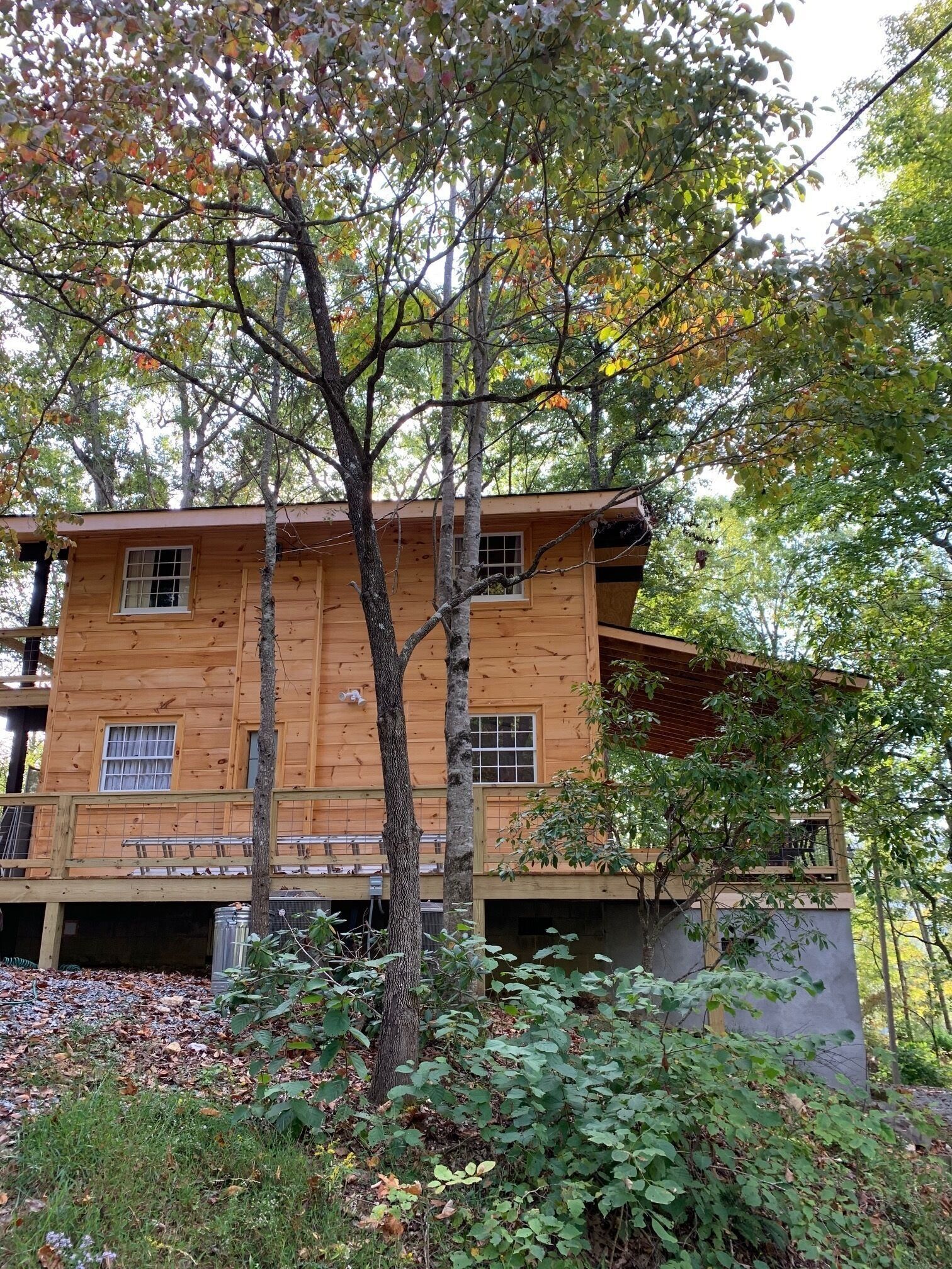 A wooden cabin with a balcony, surrounded by trees and foliage.