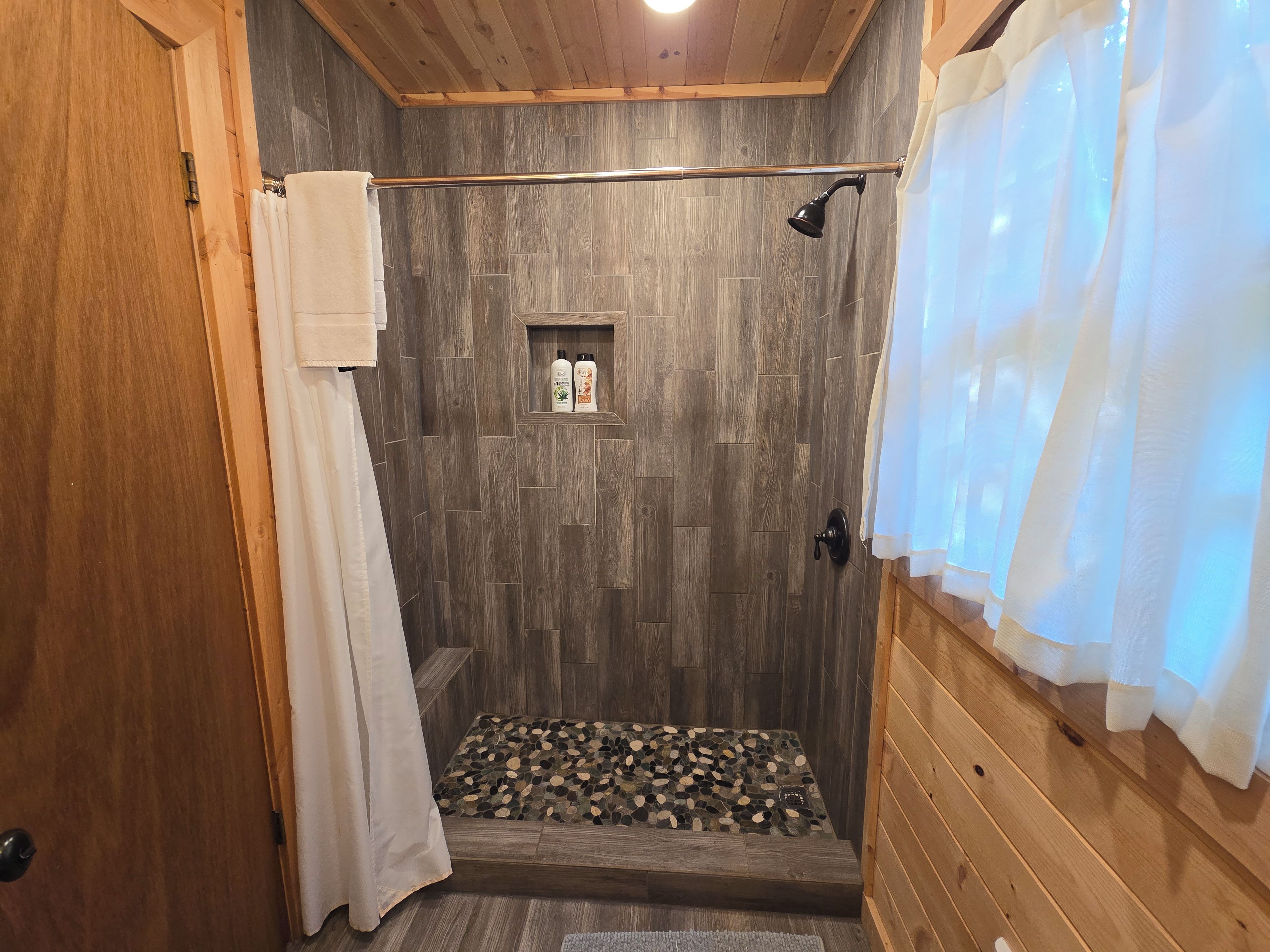 A shower area with wooden walls, a showerhead, and a shelf with toiletries.