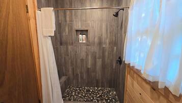 A shower area with wooden walls, a showerhead, and a shelf with toiletries.