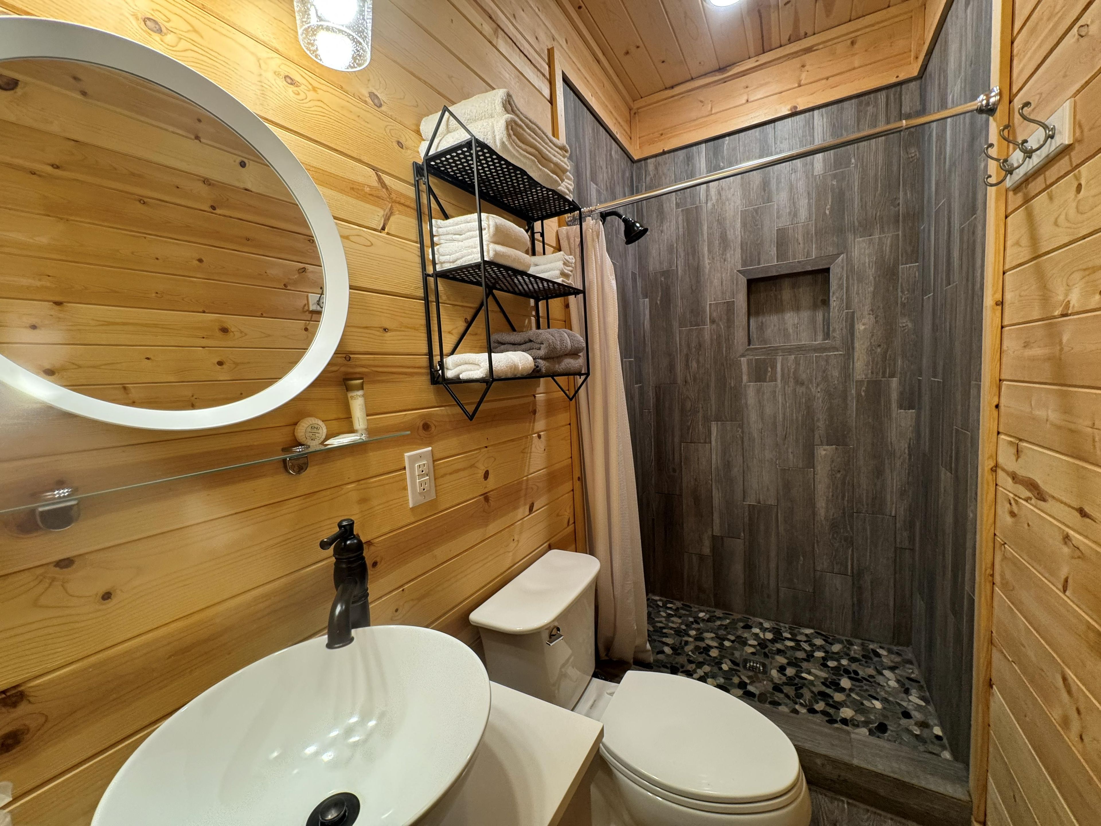 Ein Badezimmer mit Holzausstattung, einem runden Spiegel, einem Waschbecken, einer Toilette und einer Duschkabine.