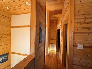 Un pasillo interior de madera con suelo de madera, una puerta y una lámpara fijada a la pared.