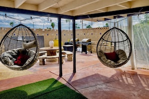 A patio area with two hanging chairs, a round table, and a grill. - Prime Location! Cozy home with pool, just minutes from the airport & Strip! (Las Vegas)