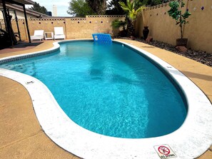 A swimming pool with a no diving sign, surrounded by a beige wall with decorative tiles, and a few lounge chairs. - Prime Location! Cozy home with pool, just minutes from the airport & Strip! (Las Vegas)
