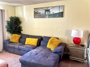A living room with a sofa, ottoman, and a lamp on a nightstand. - Prime Location! Cozy home with pool, just minutes from the airport & Strip! (Las Vegas)