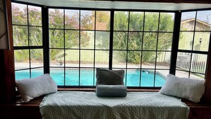 Une chambre dotée d’une grande baie vitrée donnant sur une piscine et un jardin.