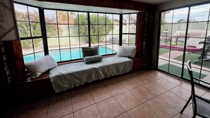 Une pièce dotée d’une grande fenêtre donnant sur une piscine, d’un banc agrémenté de coussins et d’un ventilateur de plafond.