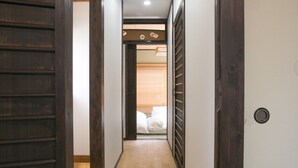 A hallway with wooden doors and a tiled floor leading to a room with a bed. - Shichihonmatsu Machiya ICHI (Kyoto)