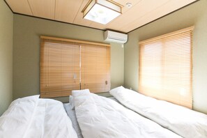 A room with two beds, wooden blinds, an air conditioning unit, and a ceiling light fixture.
