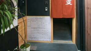 A narrow entrance with a wooden door, a small potted plant, and a red towel hanging on the wall. - Shichihonmatsu Machiya ICHI (Kyoto)