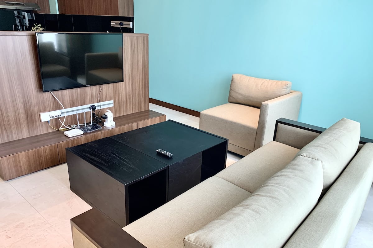 Un salon moderne avec un téléviseur à écran plat fixé à un mur en bois, une table basse noire, un canapé beige et un fauteuil assorti.