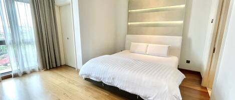 Un dormitorio moderno con una cama grande, suelo de madera y vistas al exterior a través de una ventana con cortinas.