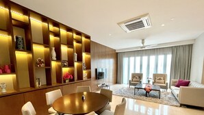 Uma sala de estar moderna com uma mesa de jantar redonda, assentos confortáveis, uma televisão de tela plana e uma grande janela com cortinas.