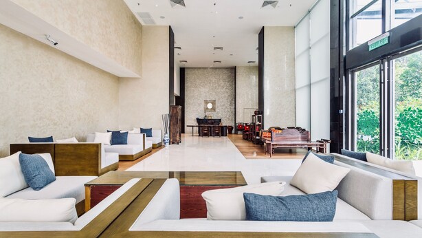 Um hall amplo com design moderno, com área de estar com sofás e uma mesa de centro, uma recepção e vista para o verde através de grandes janelas.
