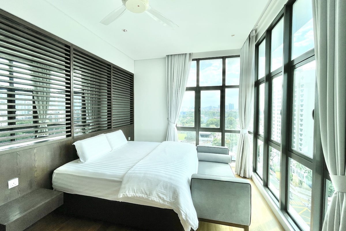 Une chambre d’hôtel moderne dotée d’un grand lit, d’une banquette intégrée et offrant une vue sur la ville grâce à de grandes fenêtres.