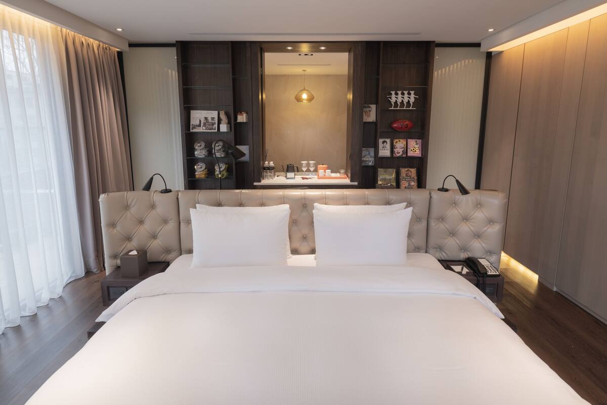 Una habitación de hotel moderna con una cama grande, una mesita de noche con lámpara, un bidet con teléfono y un televisor montado en la pared.