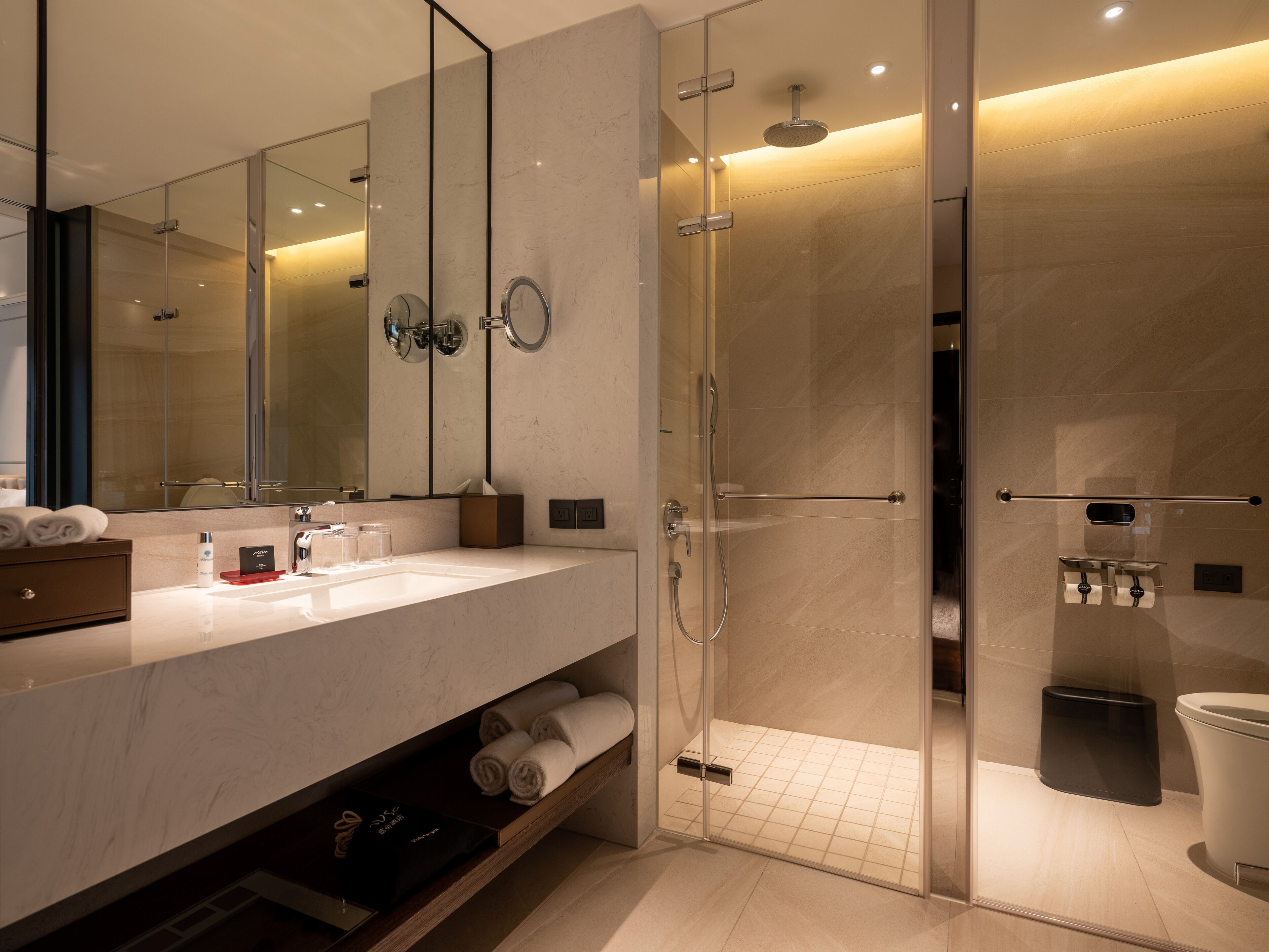 A modern bathroom with a glass-enclosed shower, a large mirror, and a marble countertop.