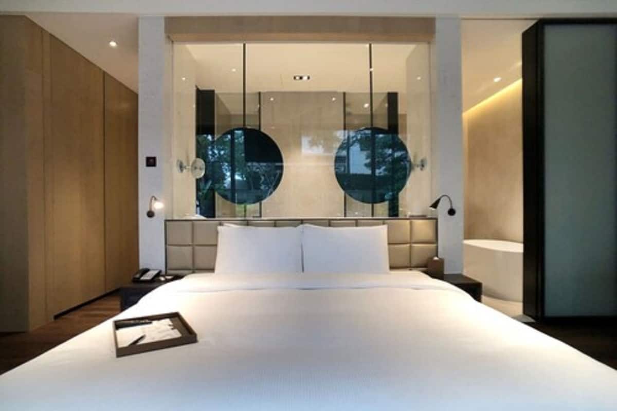 Un dormitorio moderno con una cama grande, una mesita de noche y una pared de vidrio con espejos circulares.