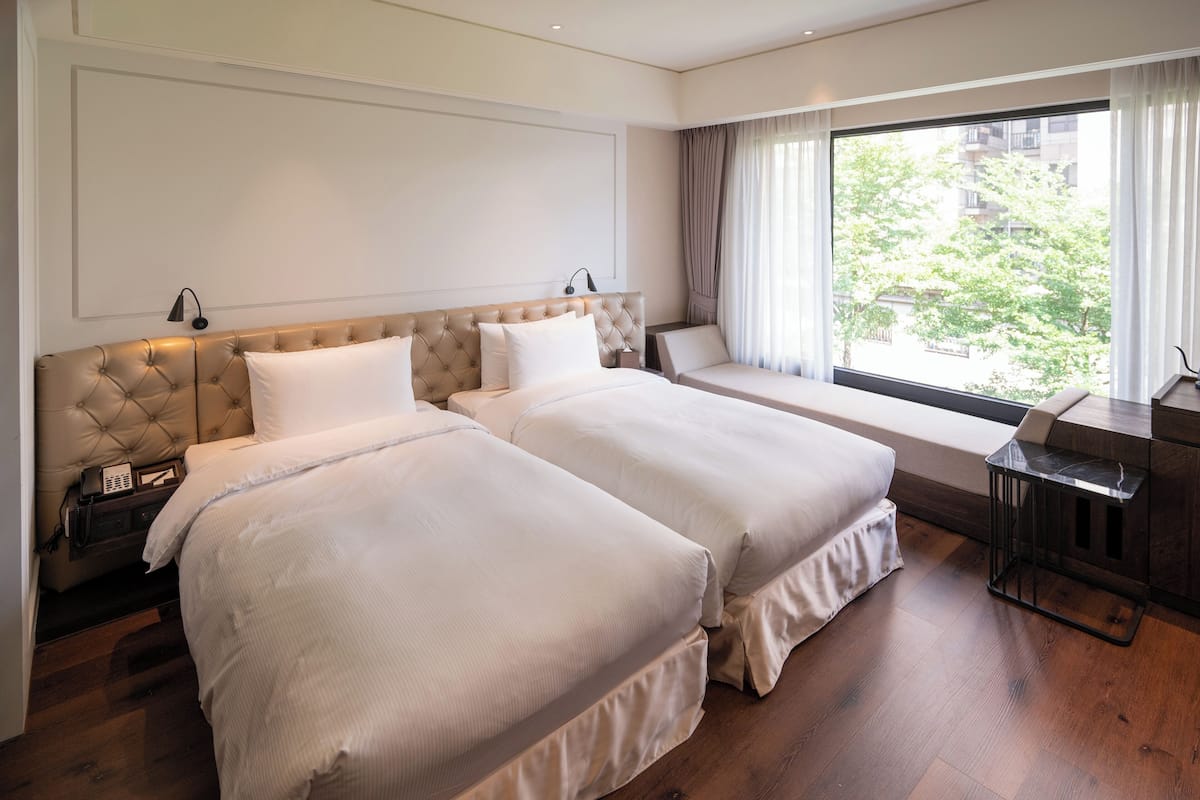 Habitación de hotel con dos camas, un escritorio y un ventanal grande con cortinas.