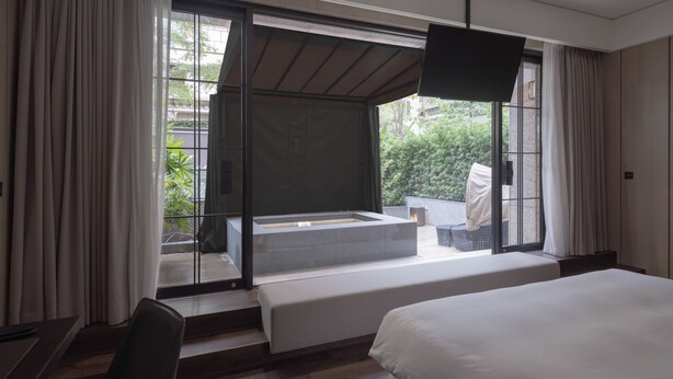 Una camera d'albergo moderna con un letto grande, un angolo salotto vicino alla finestra e vista sul verde.