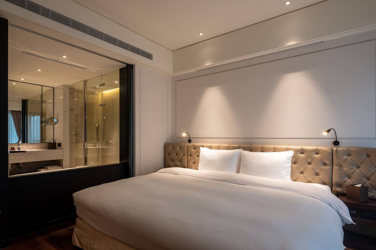 Un dormitorio moderno con una cama grande, cabina de ducha de vidrio y una mesita de noche con lámpara.