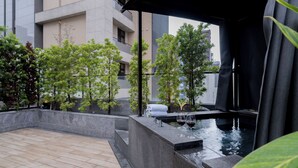 Un'area esterna moderna con pavimento in pietra, una piccola fontana e vegetazione curata.