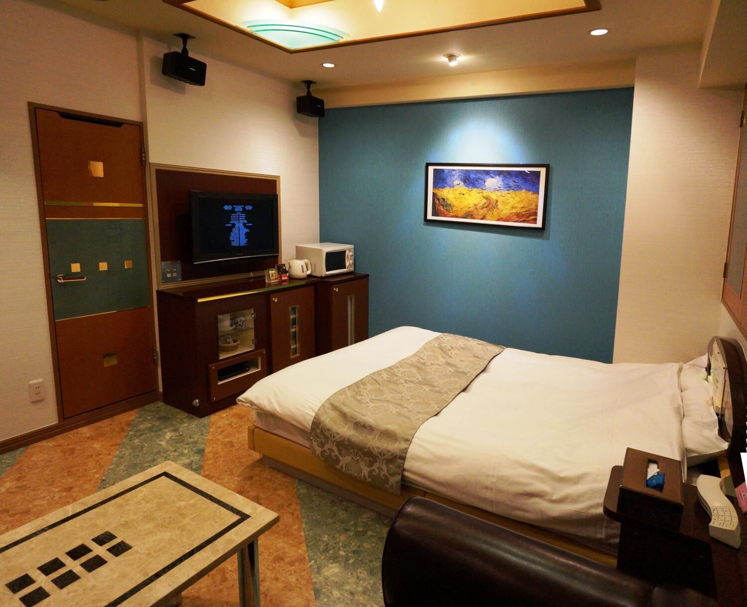 A hotel room with a bed, a television, a microwave, a cabinet, and a painting on the wall.