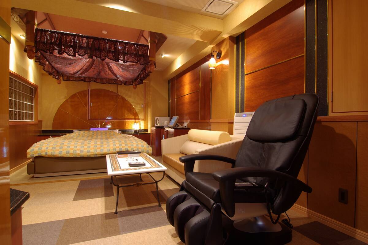 Una habitación de hotel con una cama grande, un escritorio, una silla y un sillón de masaje.
