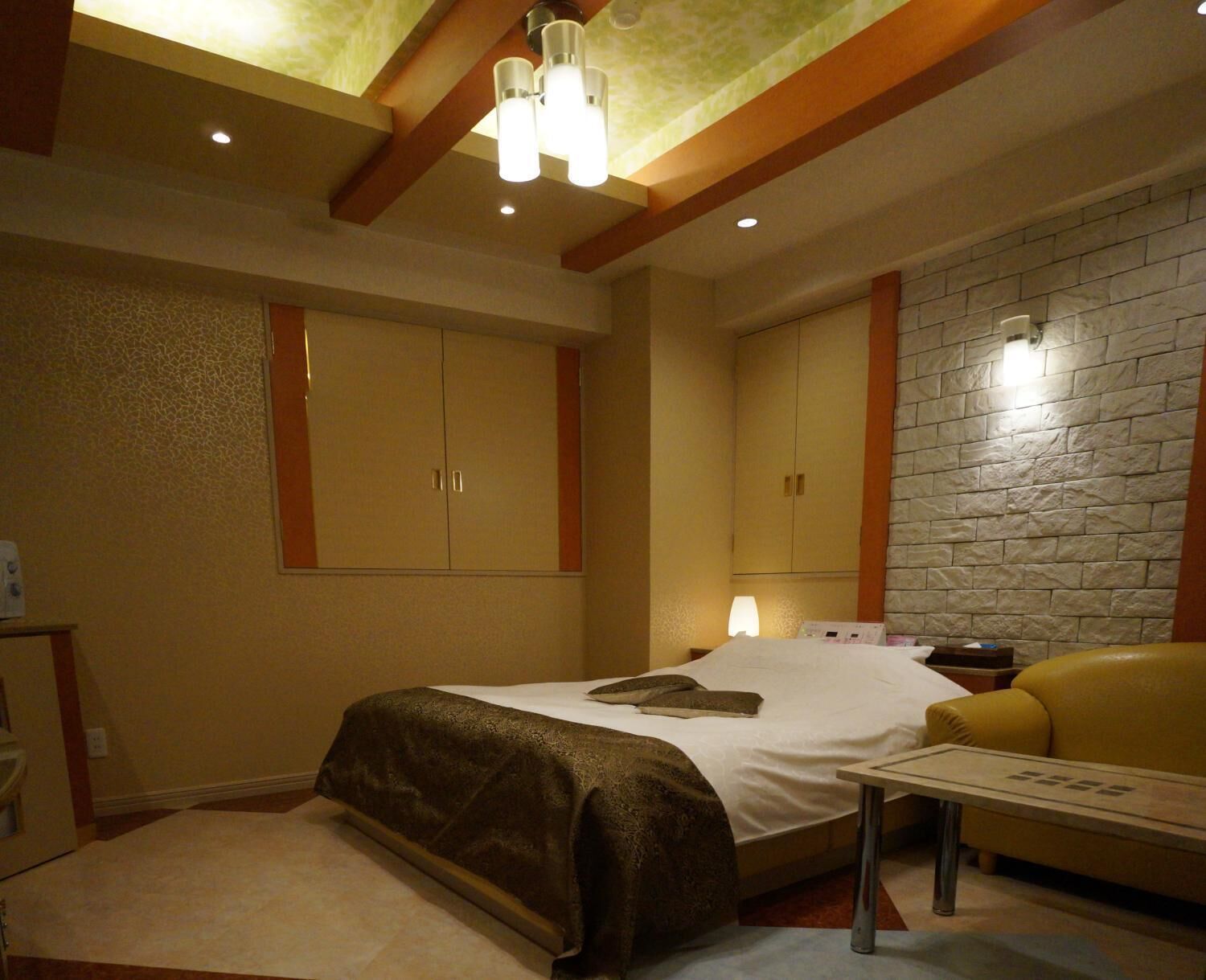 A bedroom with a bed, a nightstand, a lamp, a sofa, and a stone wall.