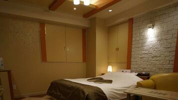 A bedroom with a bed, a nightstand, a lamp, a sofa, and a stone wall.