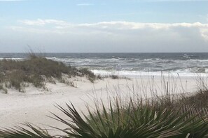 A beach with waves crashing onto the shore, sandy dunes, and sparse vegetation. - Beachside 2 bedroom 2 bathroom with Beach Views, Unit B27, fresh updates! (Gulf Shores)