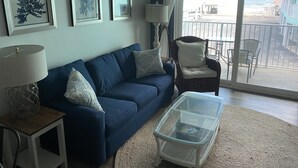 Een woonkamer met een blauwe bank, een glazen salontafel en uitzicht op het balkon.
