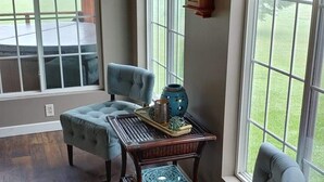 A room with a wooden ceiling, two large windows, a clock, and a table with a tray and decorative items. - Secluded Rustic Cabin (Cashton)