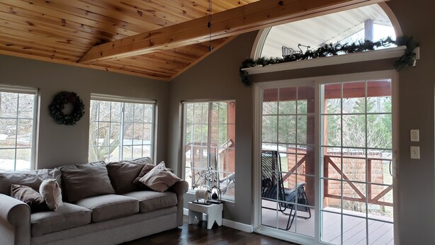 A cozy living room with a wooden ceiling, a grey sofa, and a view through a glass door to an outdoor patio. - Secluded Rustic Cabin (Cashton)