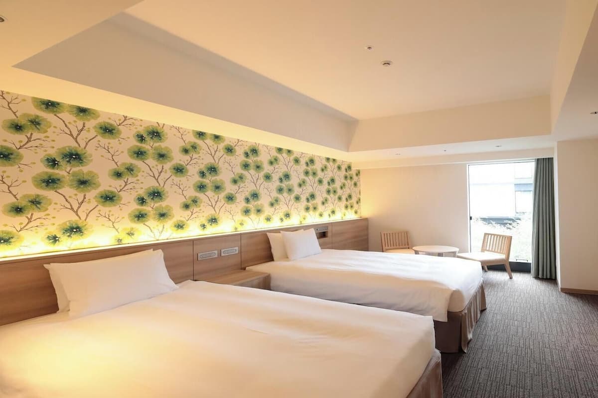 A hotel room with two beds, a TV, a small table, and a view of the outdoors.