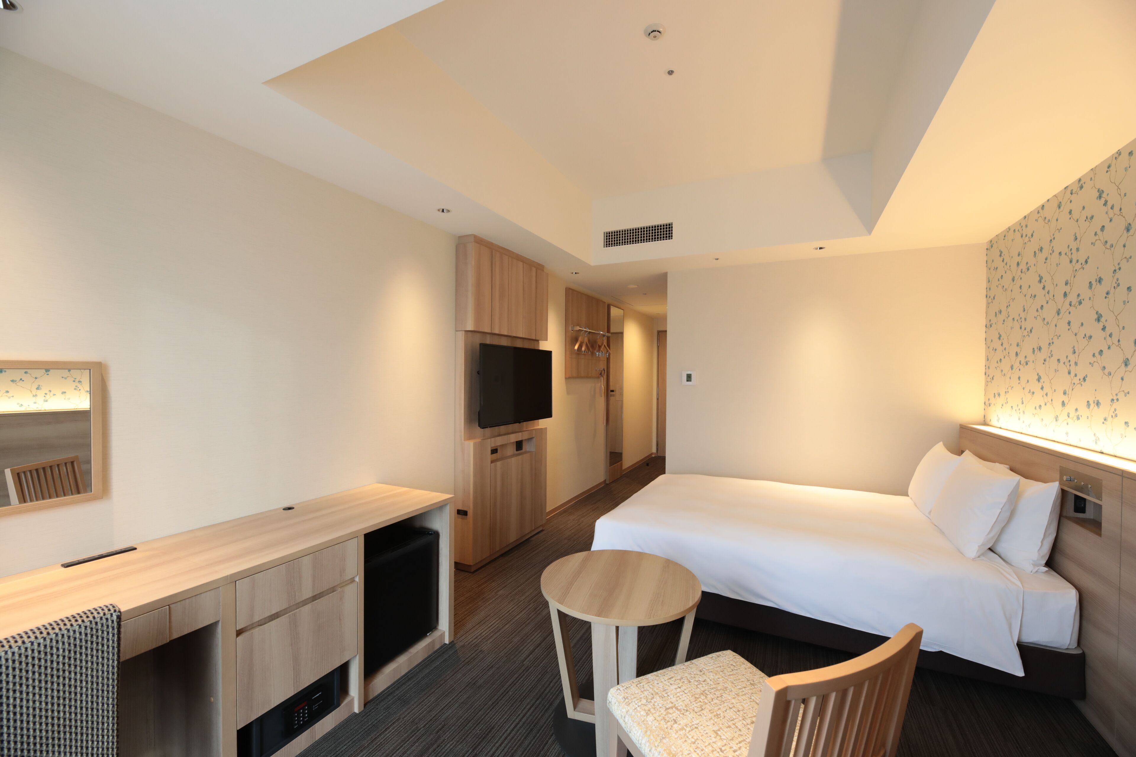 Una habitación de hotel con cama, escritorio, silla, televisor y armario.
