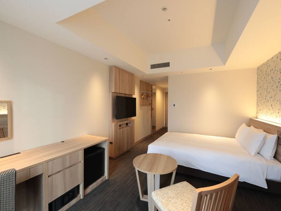 Una habitación de hotel con cama, escritorio, silla, televisor y armario.